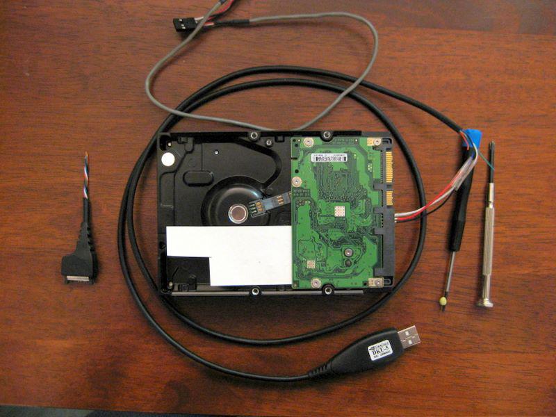 Underside of a hard disk, including the tools used for the process. USB cable, screwdriver, cardboard